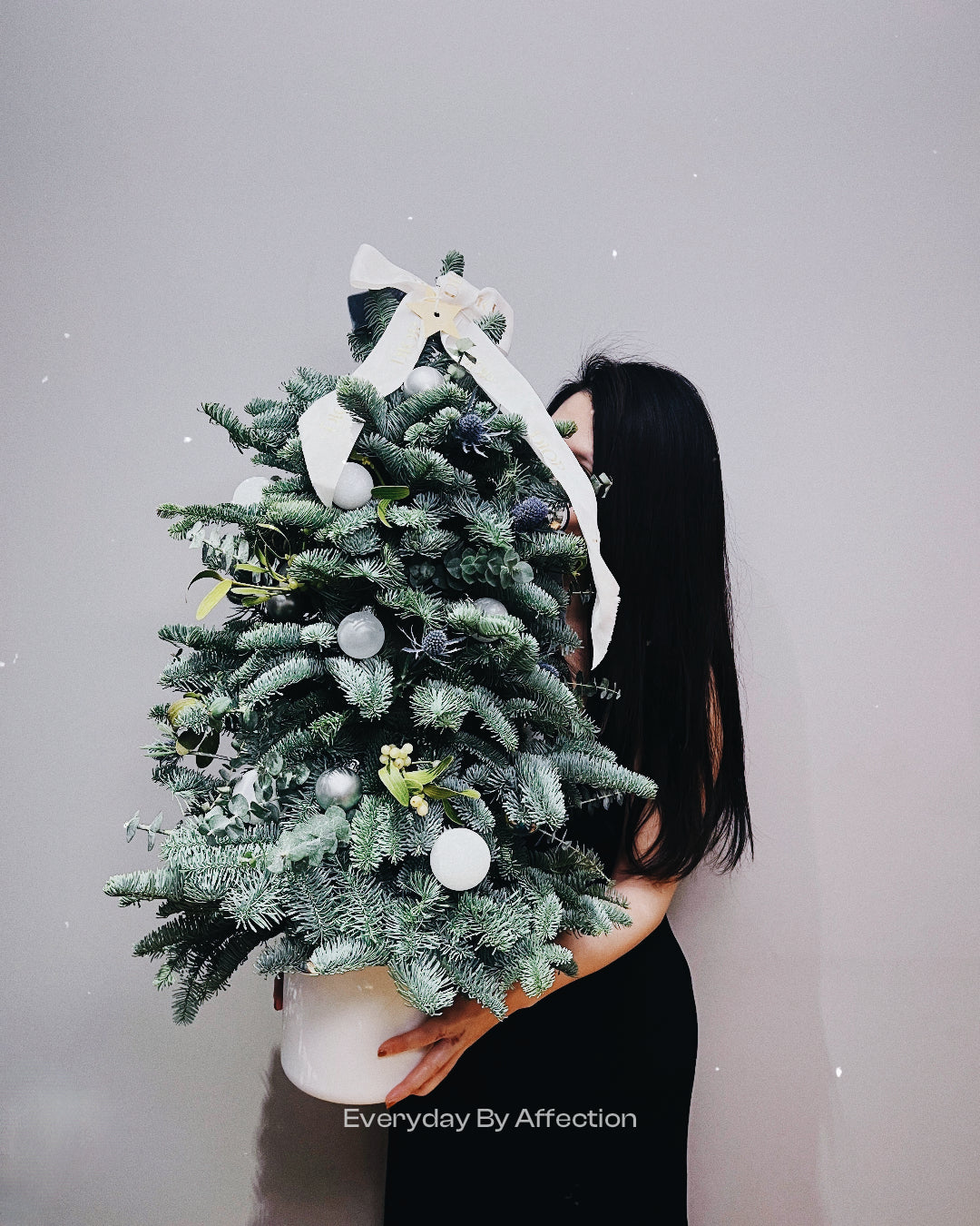 a girl holding a fresh christmas tree with ribbons and ornaments