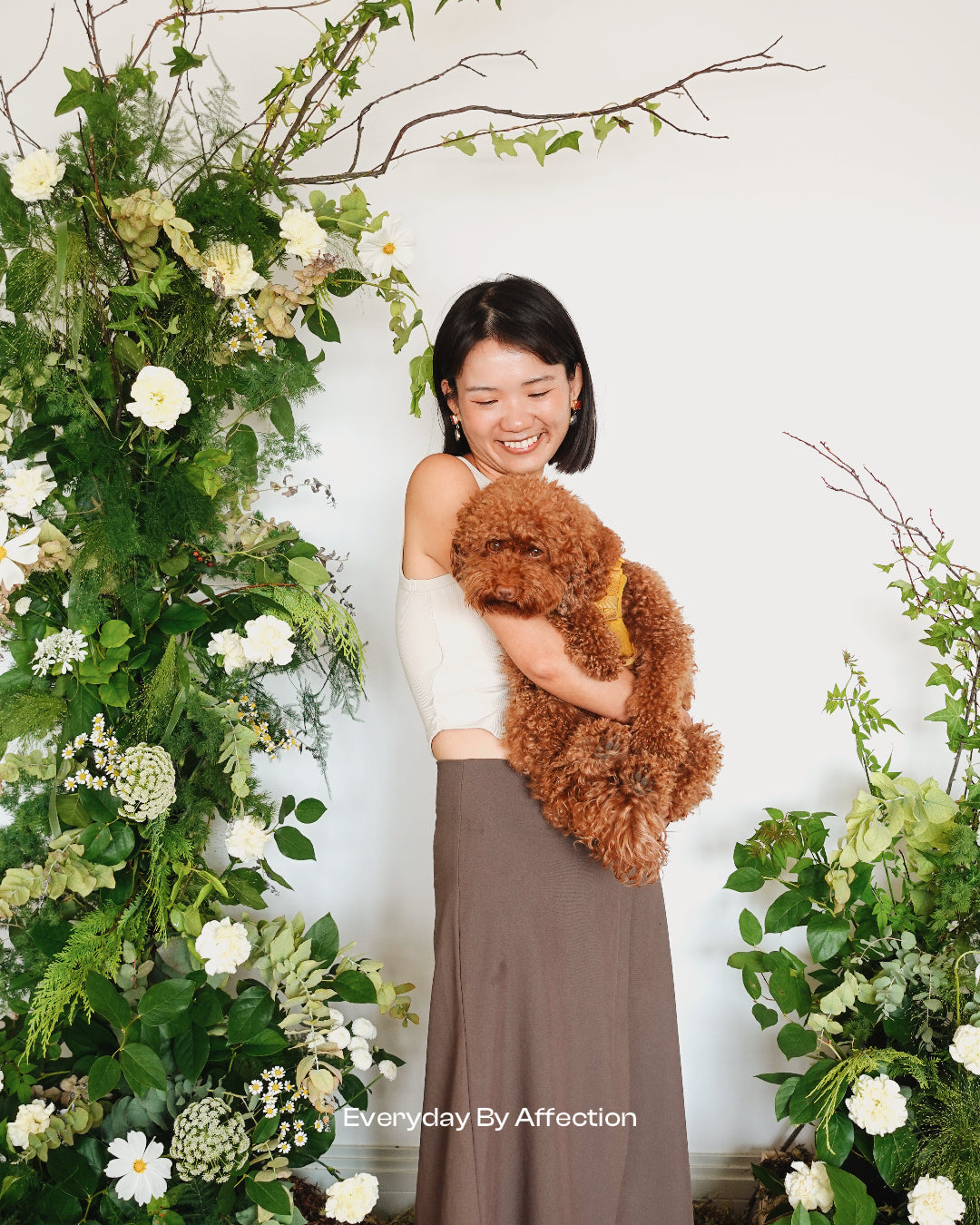 a girl hugging a dog taking pictures in front of natural flower pillar