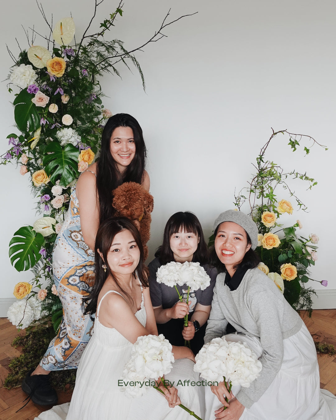girls holding white hydrangeas in front a floral pillar