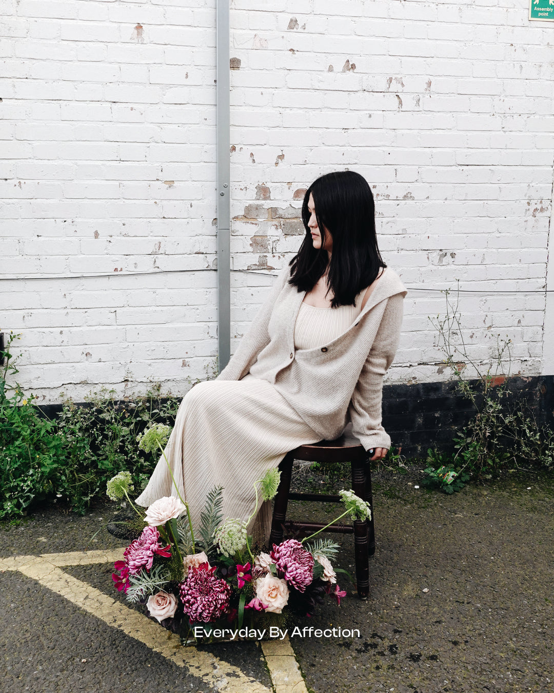 a girl sitting on a bench with flowers in front of her for fashion shoot