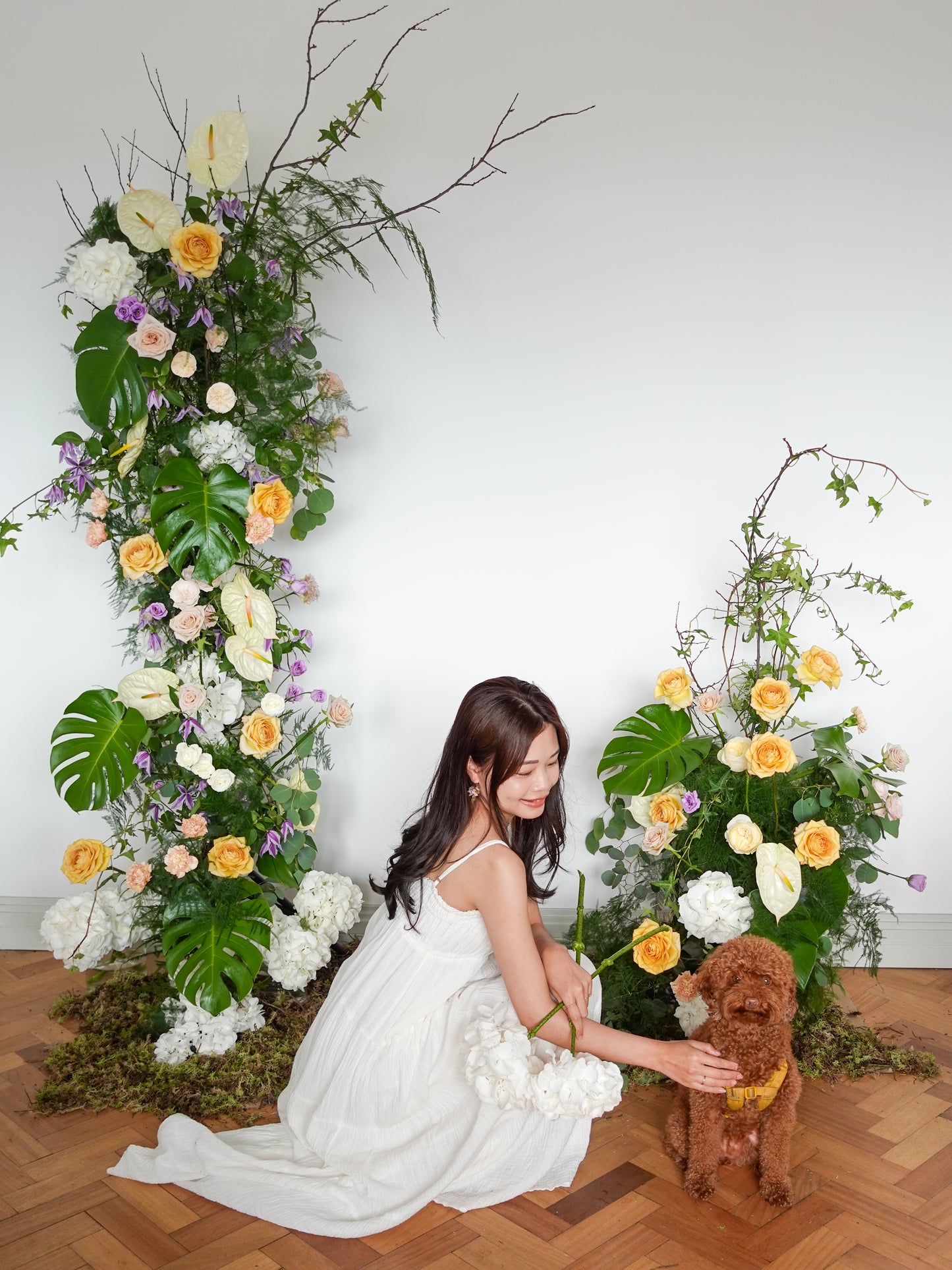 a girl and a dog in front of a natural flowy floral pillar with yellow roses and white hydrangeas and green leaves