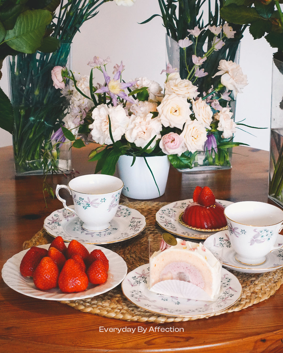 a vase flowers with cakes strawberries and tea