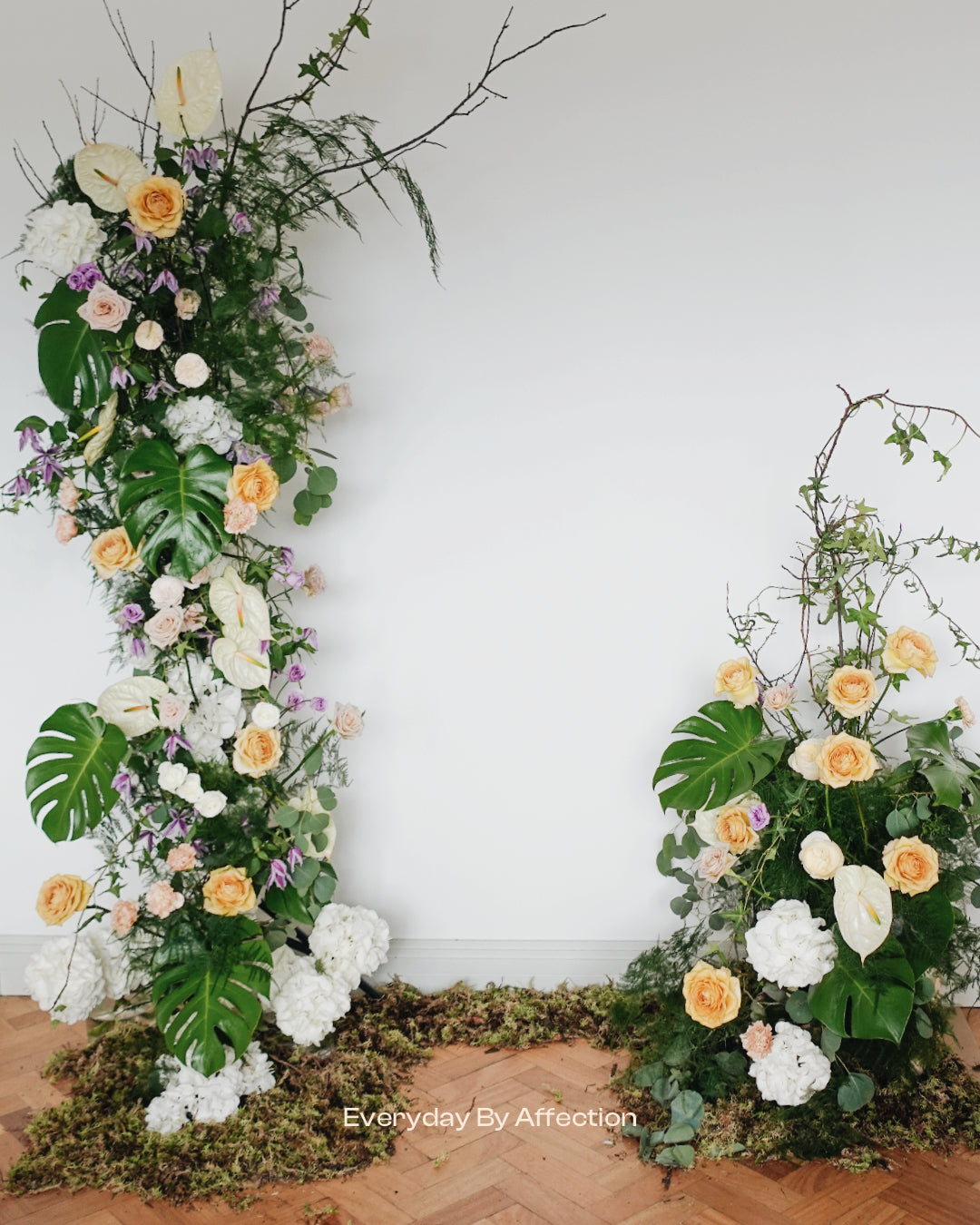 Flower Pillar in yellow roses white hydrangeas and white anthuriums with green leaves in front of a white wall